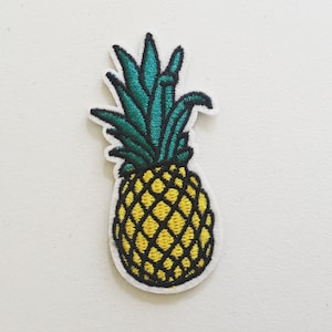 May include: A yellow pineapple with a green leafy top. The pineapple is embroidered on a white fabric.