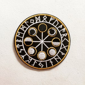 May include: Circular black embroidered patch with a gold border and white stitching. The design features a central starburst pattern with seven moon phase symbols and runic text around the edge. A unique patch.