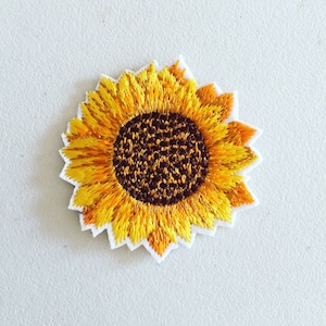 Könnte beinhalten: Ein gelber gestickter Sonnenblumen-Patch mit brauner Mitte. Die Sonnenblume ist ein beliebtes Symbol für Glück und Freude.
