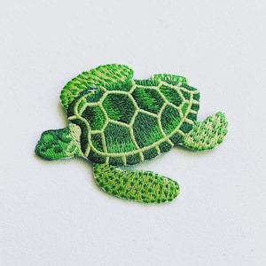 Peut inclure: Patch brodé de tortue de mer verte. La tortue est tournée vers la droite et a une carapace détaillée avec un jeu de couleurs vert et jaune.
