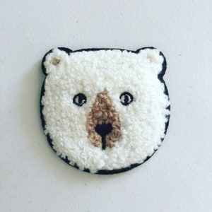 May include: White fluffy bear face patch with black eyes and a brown nose. The patch is outlined in black.