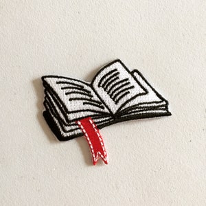 May include: An embroidered patch depicting an open book with a red bookmark. The book is open to a page with lines of text.