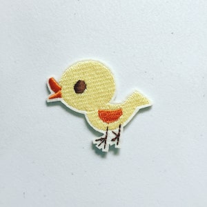 Peut inclure: Un oiseau jaune brodé avec des accents orange et des pattes brunes. L'oiseau regarde vers la gauche et a un petit œil noir.