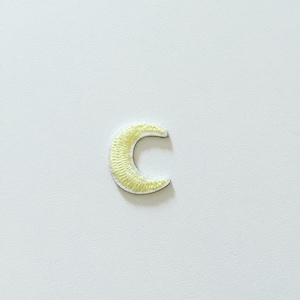 May include: A yellow crescent moon embroidered patch. The patch is outlined in white thread.