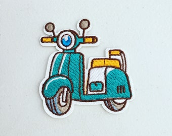 May include: A teal blue and white embroidered patch of a vintage scooter with brown handlebars and a yellow seat.