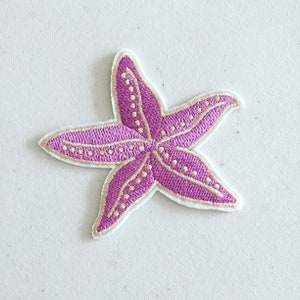 May include: A pink and gold embroidered starfish patch. The starfish is outlined in gold and has a dotted pattern.