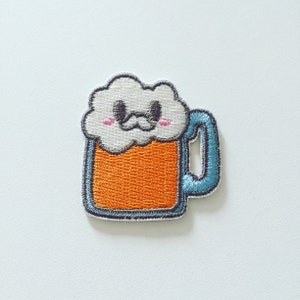 Könnte beinhalten: Ein Cartoon-Bierkrug mit einem weißen, schaumigen Kopf und einem blauen Henkel. Der Krug hat ein fröhliches Gesicht mit einem Schnurrbart und rosa Wangen.