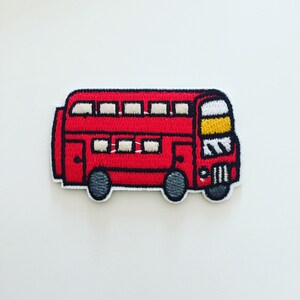 Peut inclure: Patch brodé représentant un bus à impériale rouge avec des fenêtres blanches et des détails jaunes.