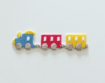 May include: A blue, red, and yellow embroidered train applique with three cars. The engine car has a yellow top and the caboose car is yellow. The middle car is red.