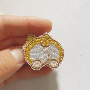 Könnte beinhalten: Ein weißer und gelber gestickter Aufnäher mit dem Hinterteil eines Hundes und einem Schwanz.