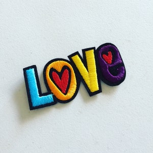 Könnte beinhalten: Ein bunter gestickter Aufnäher mit dem Wort "LOVE" in Regenbogenfarben. Jeder Buchstabe hat ein kleines Herz im Inneren.