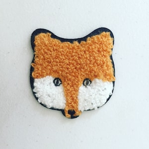 Könnte beinhalten: Ein braunes und weißes Fuchsapplikation mit einer flauschigen Textur. Der Fuchs hat schwarze Augen und eine schwarze Nase.