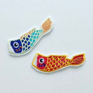 Könnte beinhalten: Zwei gestickte Fisch-Patches, einer blau und grün mit orangefarbenen Flossen, der andere rot und gelb mit roten Flossen.