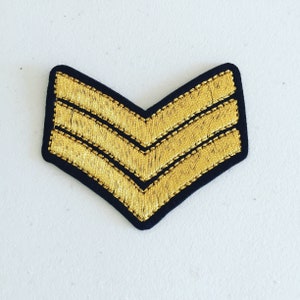 May include: A gold embroidered chevron patch with three stripes on a black felt backing.