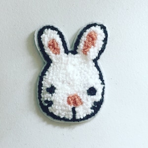 Könnte beinhalten: Weißer, flauschiger Hasen-Patch mit schwarzem Umriss und rosa Ohren und Nase.