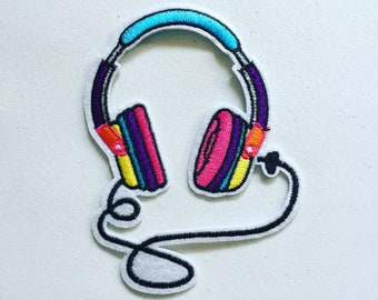 May include: A colorful embroidered patch of a pair of headphones with a cord. The headphones are purple, pink, yellow, and blue. The cord is black and white.