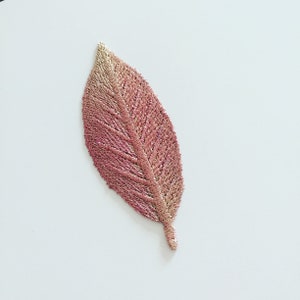 May include: An embroidered leaf in shades of pink and gold, featuring a detailed vein pattern.