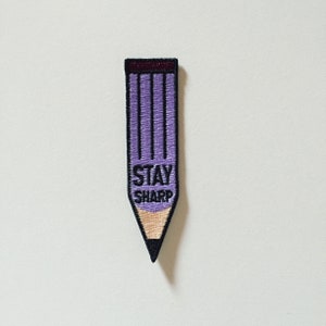 May include: Purple embroidered iron-on patch shaped like a pencil with the text "STAY SHARP" in black.