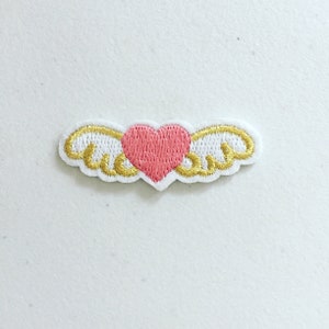 May include: An embroidered patch featuring a pink heart with gold wings.