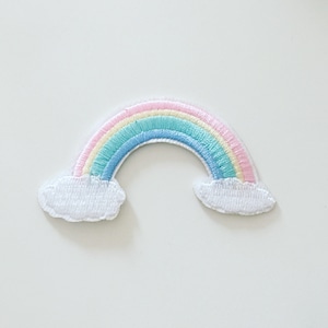 May include: An embroidered patch featuring a pastel rainbow with clouds. The rainbow is pink, yellow, light blue, and dark blue. The clouds are white.