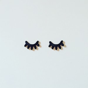 Può includere: Due ciglia finte in feltro nero, ciascuna con una forma curva, sono posizionate su uno sfondo bianco.