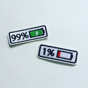 Pode incluir: Dois patches bordados para passar a ferro que representam ícones de bateria. Um patch mostra uma bateria a 99% com um raio, o outro mostra uma bateria a 1% com uma barra vermelha.