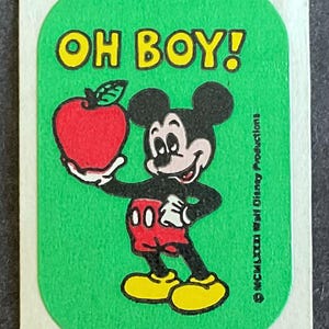 May include: A green sticker with a yellow border featuring Mickey Mouse holding a red apple. The text "OH BOY!" is printed in yellow at the top of the sticker. The copyright information "©MCMLXXXI Walt Disney Productions" is printed in black at the bottom right corner of the sticker.