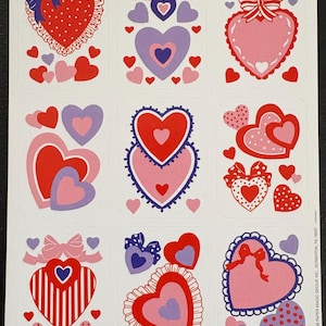 May include: Sheet of heart-shaped stickers in various designs. The stickers feature red, pink, and purple hearts with bows, polka dots, and scalloped edges. Some hearts have striped patterns. A few smaller hearts are scattered around the larger ones.