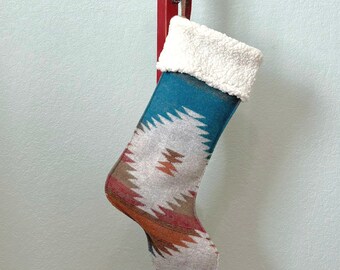 May include: A turquoise, red, and white patterned Christmas stocking with a white faux fur cuff hanging on a red wooden stocking holder.