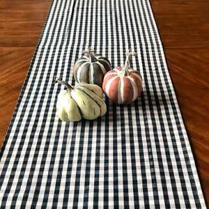 May include: Three decorative gourds in various colors and patterns, including brown, green, and orange, are arranged on a black and white checkered table runner.