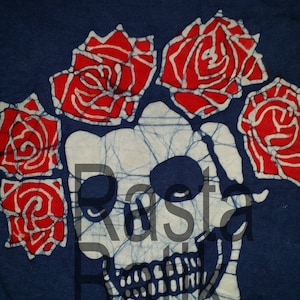 May include: Navy blue t-shirt featuring a white skull design with red roses. The skull and roses are outlined in white. The text "Rasta Batik" is printed on the shirt in white. The shirt has a crew neck.
