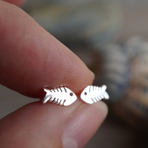 May include: A pair of silver fishbone stud earrings. The earrings are small and delicate, and they are perfect for adding a touch of whimsy to any outfit.