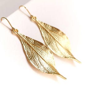 May include: A pair of gold leaf-shaped dangle earrings. The earrings are made of metal and have a textured surface.