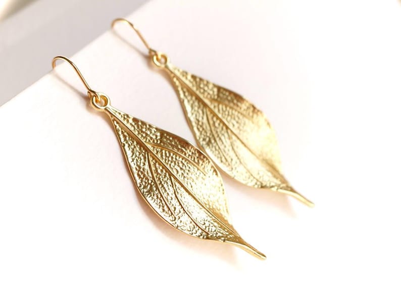 May include: A pair of gold leaf-shaped dangle earrings. The earrings are made of metal and have a textured surface.