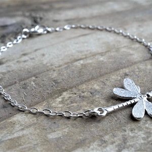 May include: A silver chain bracelet with a dragonfly charm. The dragonfly is detailed with textured wings.