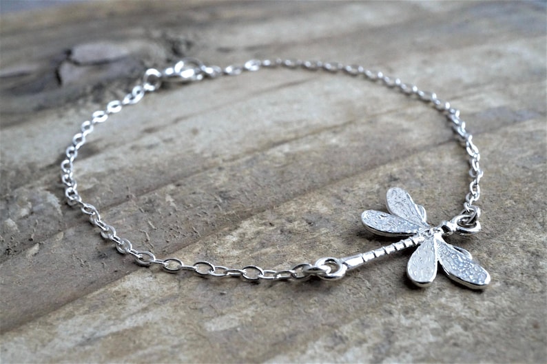 May include: A silver chain bracelet with a dragonfly charm. The dragonfly is detailed with textured wings.