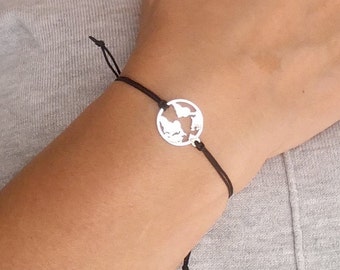 May include: A black string bracelet with a silver charm in the shape of a world map.