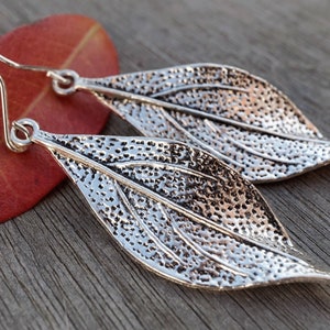 May include: A pair of silver leaf-shaped earrings with a textured surface.
