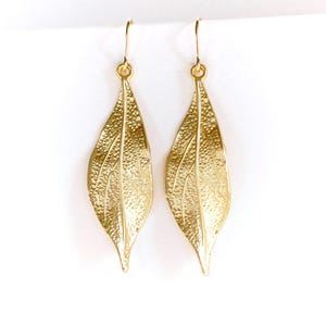 May include: A pair of gold leaf-shaped dangle earrings. The earrings are made of metal and have a textured surface.