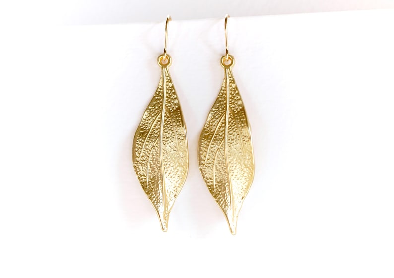 May include: A pair of gold leaf-shaped dangle earrings. The earrings are made of metal and have a textured surface.