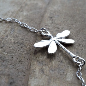 May include: A silver chain necklace with a dragonfly pendant. The dragonfly is detailed and has a long, thin body.