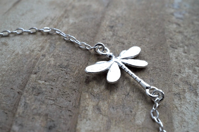 May include: A silver chain necklace with a dragonfly pendant. The dragonfly is detailed and has a long, thin body.