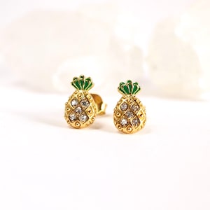 Könnte beinhalten: Ein Paar goldene Ananas-Ohrringe mit grünen Emaille-Oberteilen und klaren Strass-Akzenten.