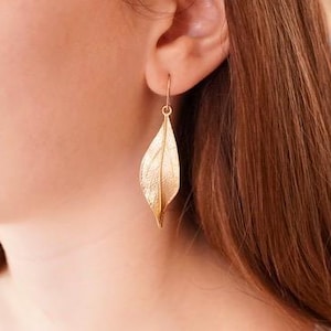 May include: Gold leaf earrings with a delicate, textured design. The earrings are dangle style and feature a single leaf shape.