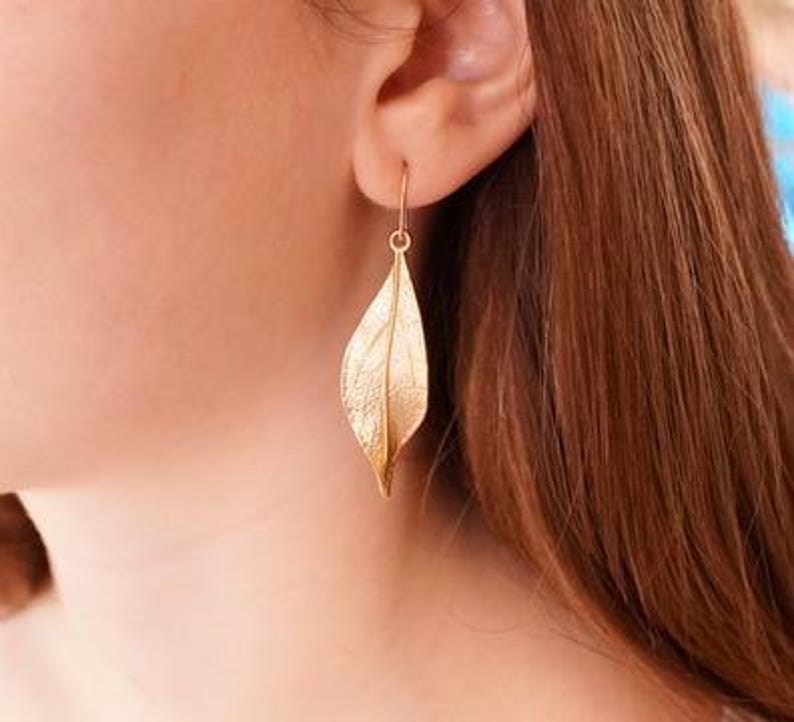 May include: Gold leaf earrings with a delicate, textured design. The earrings are dangle style and feature a single leaf shape.