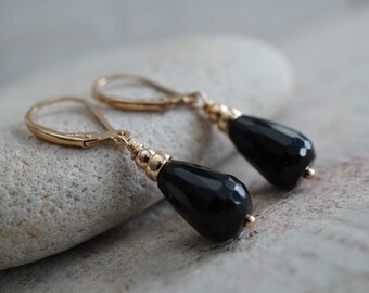 May include: A pair of gold dangle earrings with black teardrop-shaped gemstones.