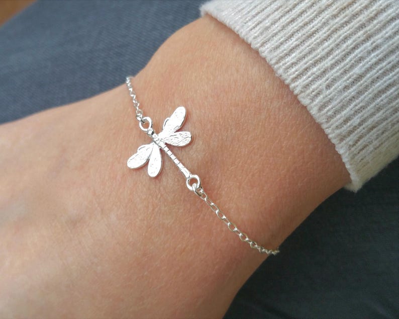 May include: A silver chain bracelet with a delicate dragonfly charm. The dragonfly has detailed wings and a textured finish.
