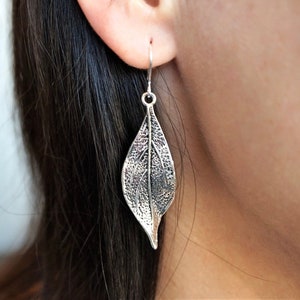 May include: Silver leaf-shaped dangle earrings. The earrings are detailed with a textured leaf design.