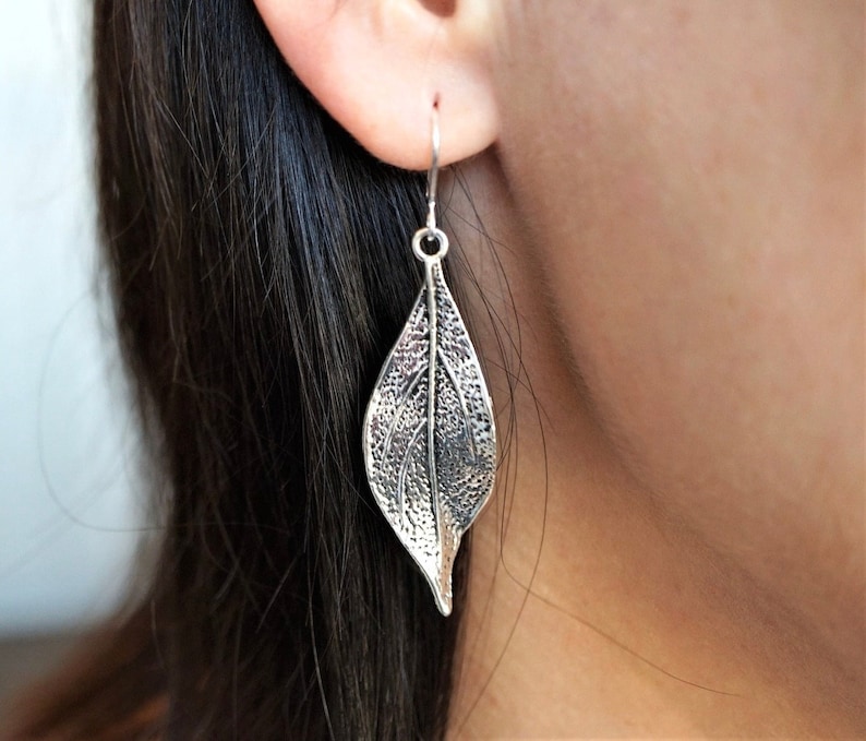 May include: Silver leaf-shaped dangle earrings. The earrings are detailed with a textured leaf design.