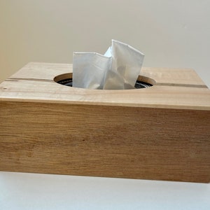 May include: A wooden tissue box holder with a natural wood finish. The box has a cutout for tissues and is made of solid wood.